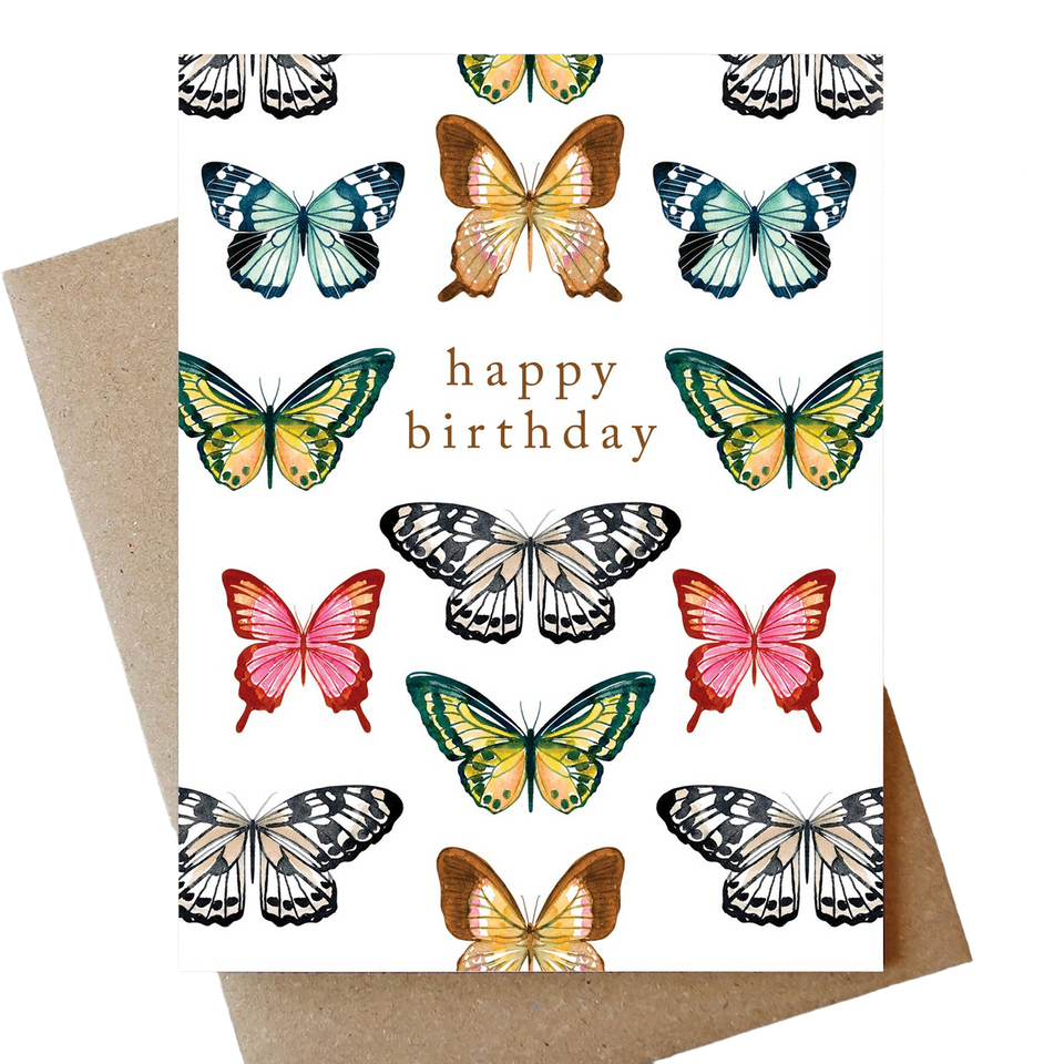 A square birthday card with a white background printed with multiple colorful butterfly illustrations and the words 'happy birthday' in brown lettering, shown with a kraft envelope behind it on a white background.