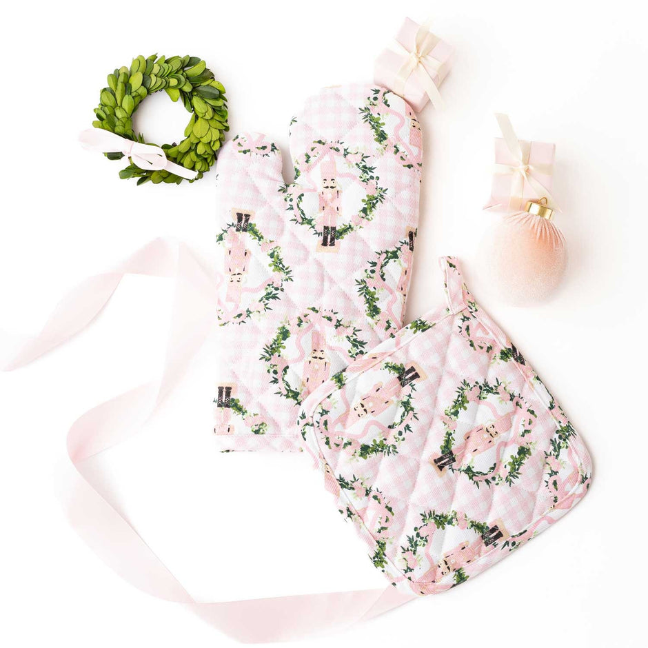 Pink gingham oven mitt set with nutcracker and greenery print, displayed with wreath and ornaments