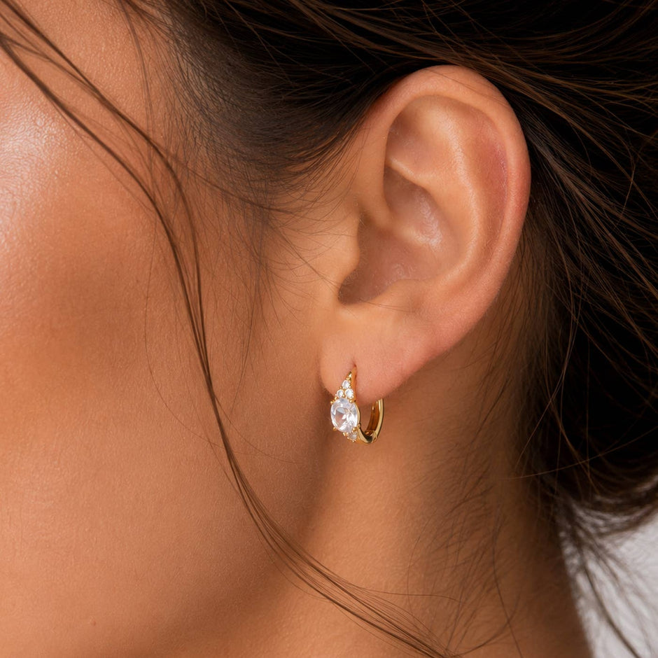 Gold marquise CZ huggie earrings worn on model's ear, showcasing elegant crystal stone design