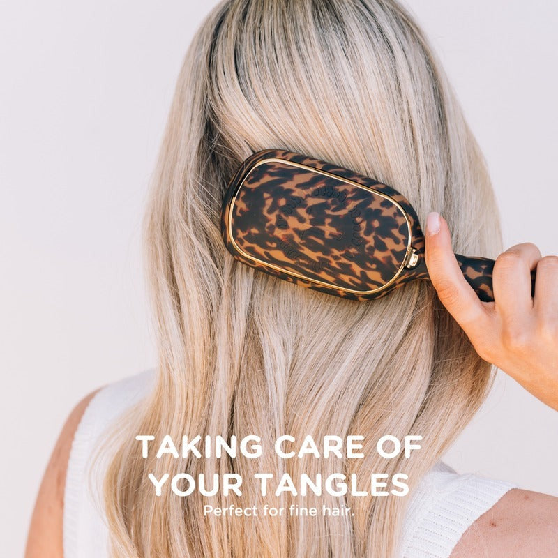 Woman using tortoise detangler hair brush on long blonde hair against white background