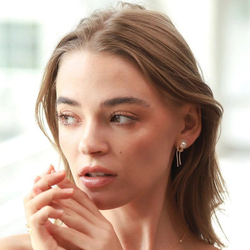 Woman wearing TAI Jewelry knotted chain pearl earrings in gold