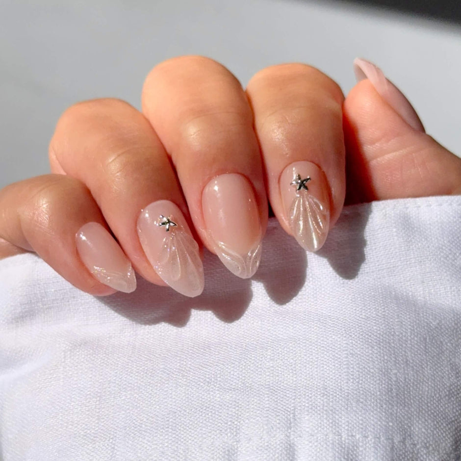 Almond-shaped nails with nude polish, delicate shell and star design details on model hand