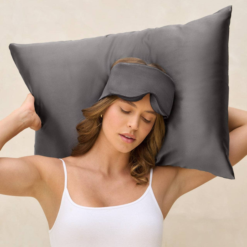Woman wearing charcoal contour eye mask while holding pillow behind head