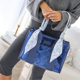 Woman holding blue jelly tote bag with floral print handles in styled indoor setting