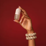 Hand holding Kitsch Warm Sugar hair perfume against red background with hair scrunchies