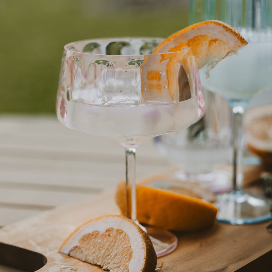 Outdoor plastic coupe glass with orange slice garnish and fresh citrus on wooden table