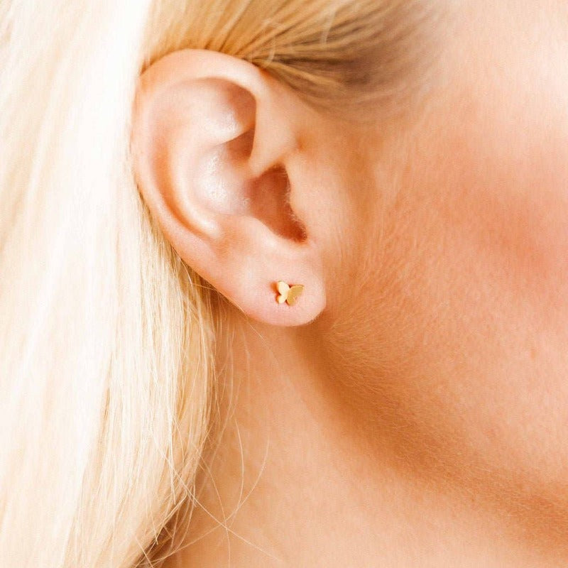 Gold butterfly stud earrings worn on model's ear with blonde hair