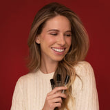 Woman holding hair perfume bottles, smiling against red background