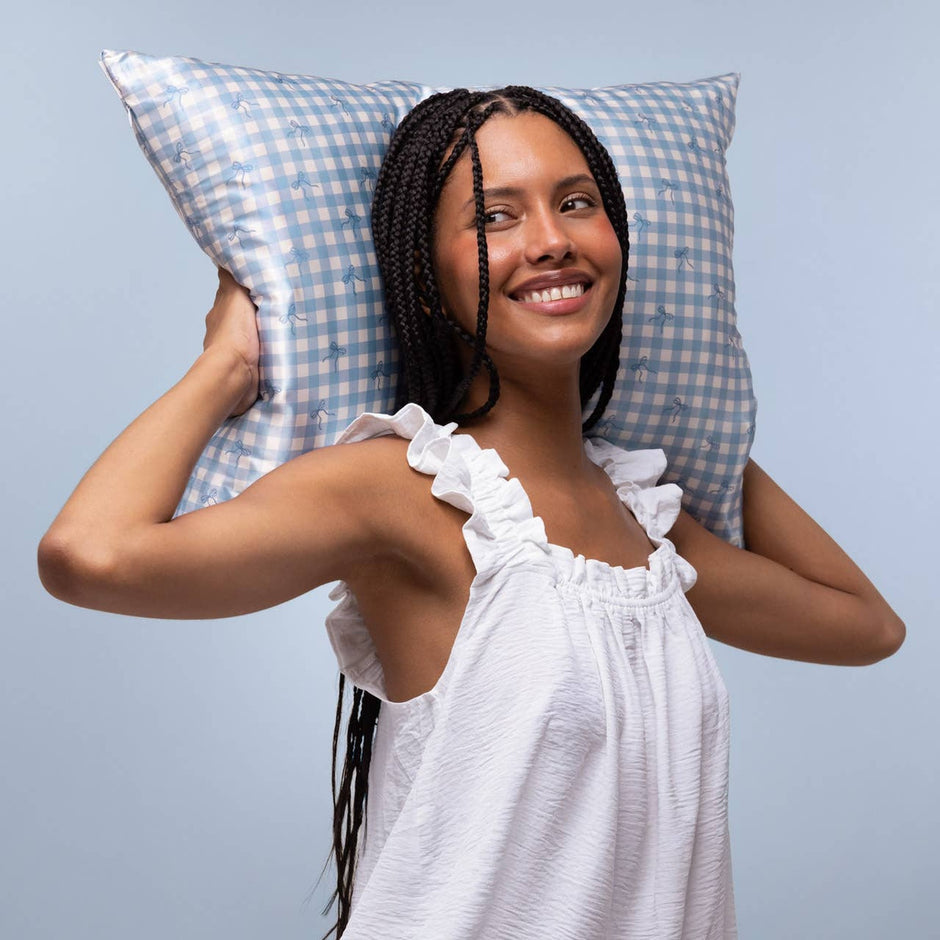 Woman holding blue gingham satin pillowcase against shoulder, smiling at camera