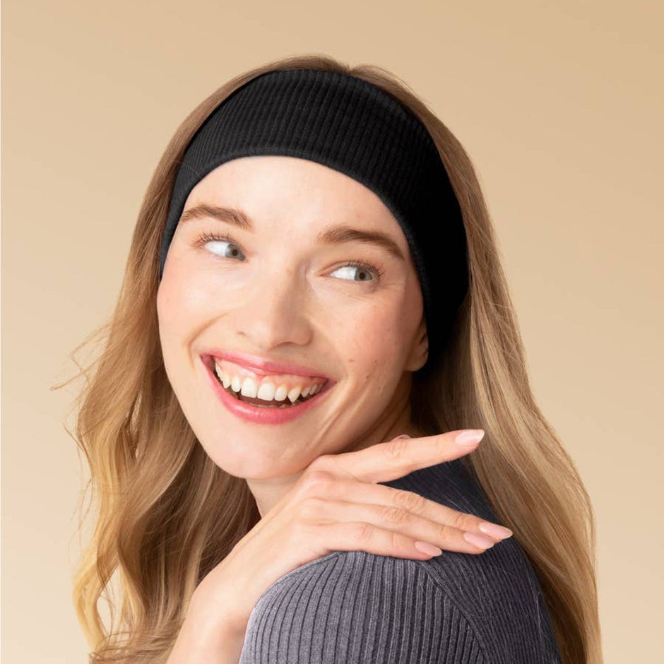 Woman wearing black ribbed elastic headband with long brown hair against neutral background