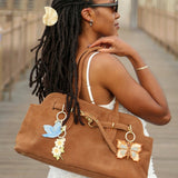 Hand-painted daisy bag charm and keychain attached to tan leather tote, styled on model