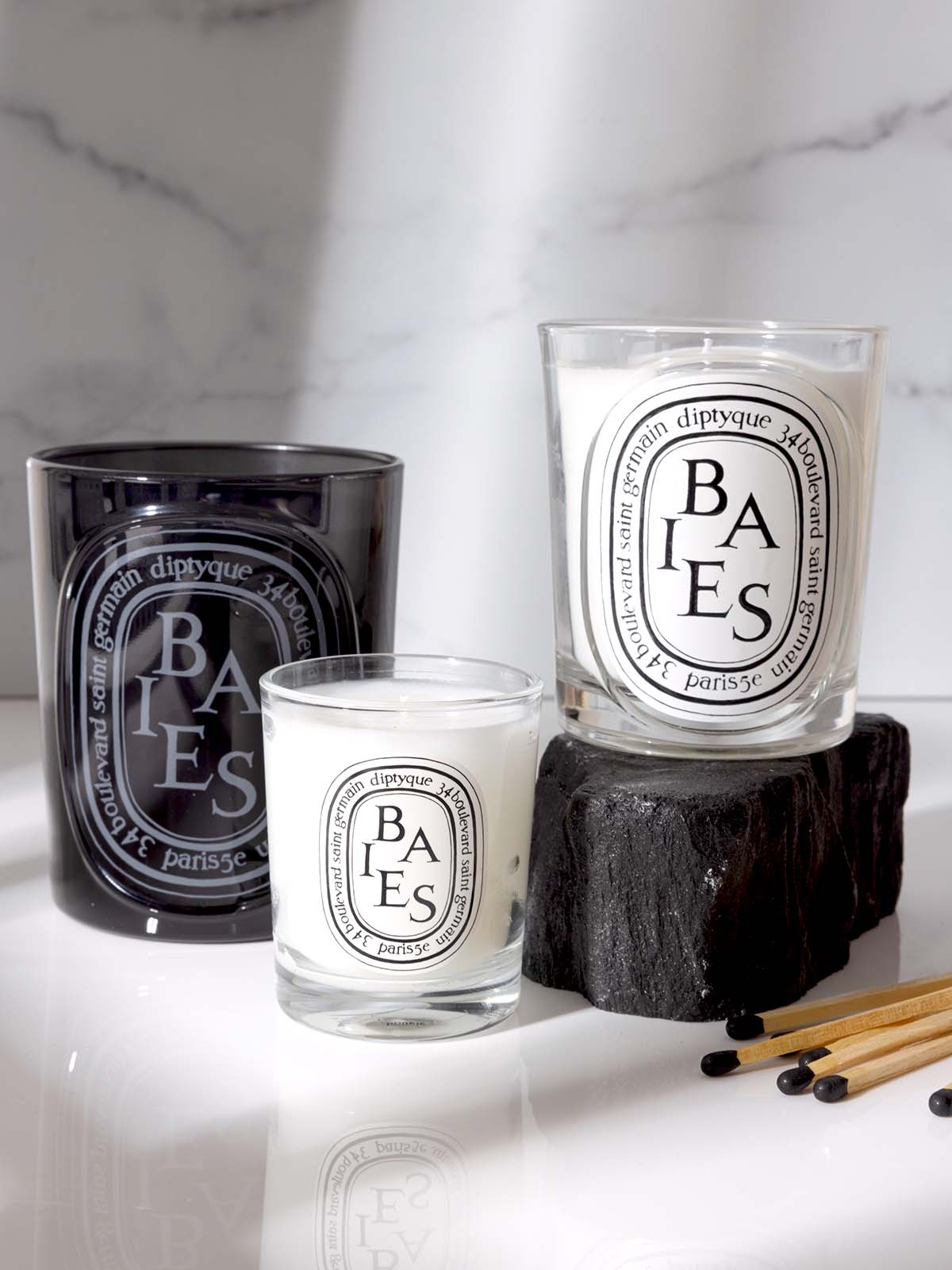 Three Baies scented candles from Diptyque arranged on a white marble background.