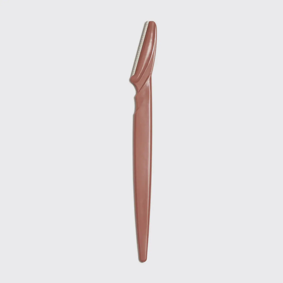 Brown dermaplaner tool on a light gray background