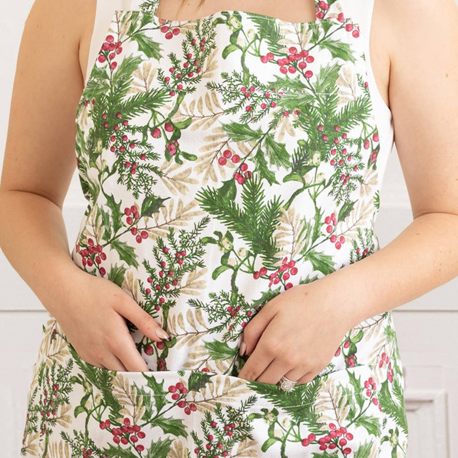 Woman wearing a white apron with woodland berry floral print featuring green leaves and red berries