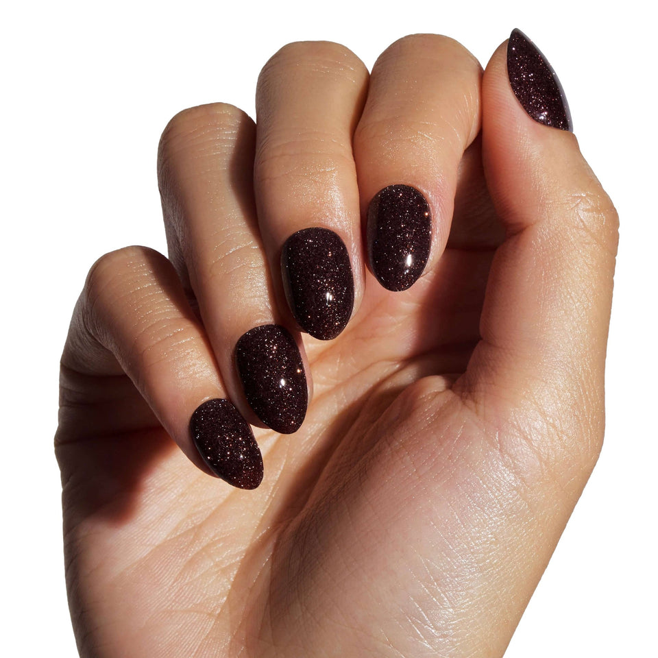 Hand displaying dark brown sparkly press-on nails with almond and stiletto shapes