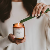 Woman holding Fraser Fir candle by Sweet Water Decor, lighting it with green rechargeable lighter