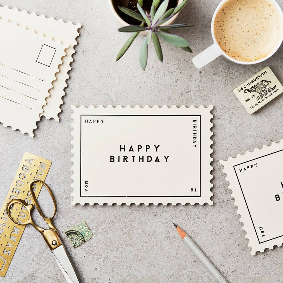 Katie Leamon Happy Birthday greeting card styled with coffee, stamps, scissors, and succulent on gray background