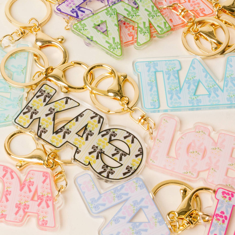 Colorful sorority letter acrylic keychains with floral patterns and gold hardware displayed on white background
