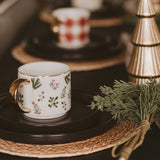 Holiday Greenery Coffee Mug displayed on black table with festive decorations and evergreen branches