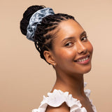 Woman wearing haze blue satin sleep scrunchie in updo hairstyle against neutral background