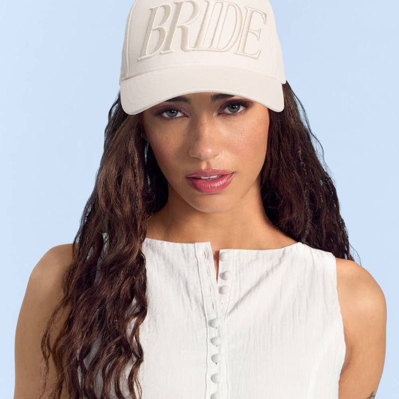 Woman wearing cream Bride trucker hat and white top against blue background