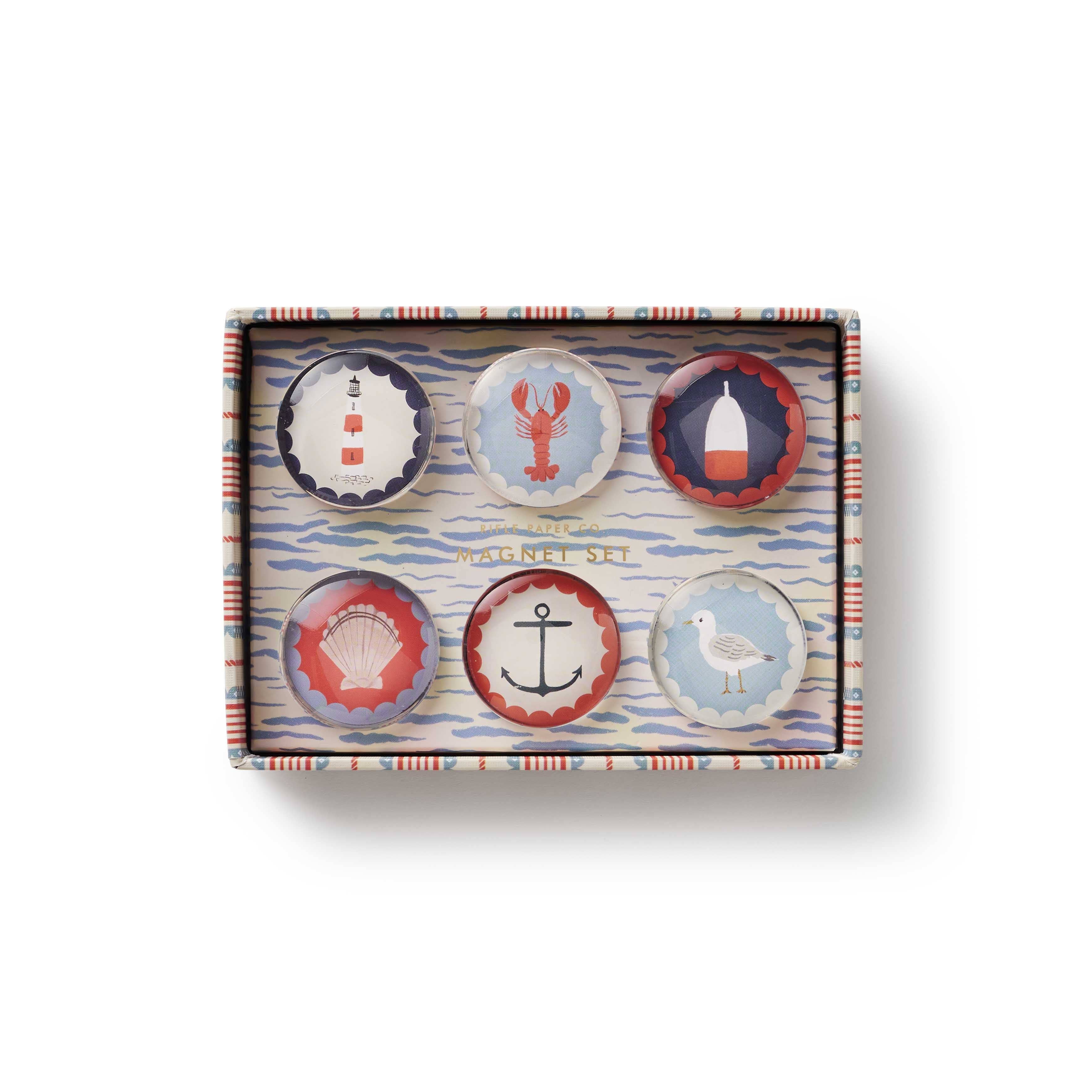 Set of six decorative buttons in a box with nautical designs on a white background