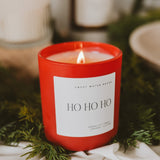 Red Ho Ho Ho scented soy candle by Sweet Water Decor surrounded by fresh evergreen branches