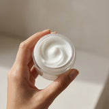 Hand holding open jar of MOTHER MOTHER Magnesium Cream showing creamy white texture