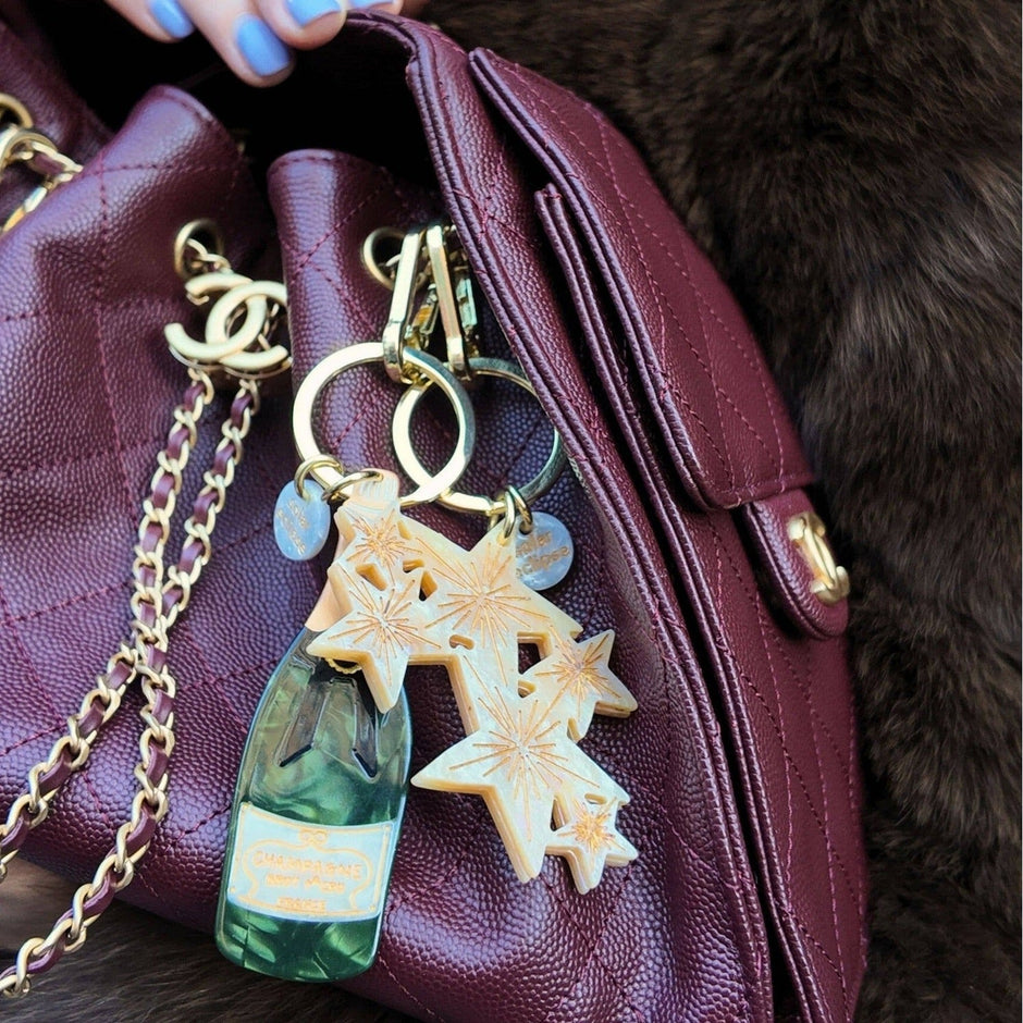 Hand-painted champagne bottle bag charm with star design attached to burgundy leather handbag