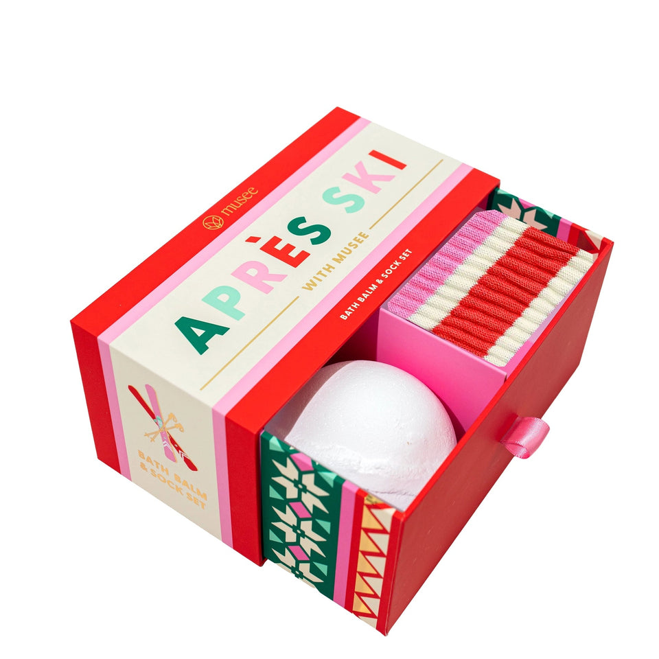 An open red and cream Après Ski with Musee gift set, containing a white bath bomb and pink and red socks, shown on a white background.