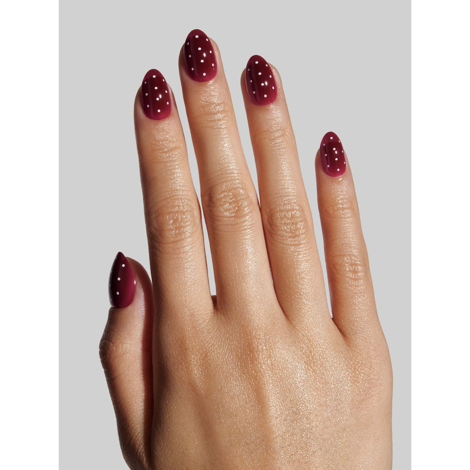 Berry polka dot press-on nails displayed on model's hand against neutral background