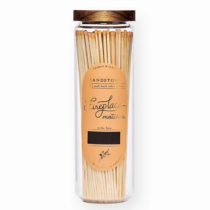 Sandstone, tall glass apothecary jar of burnt orange tipped fireplace matches with acacia wood lid and gold foil label on a white background