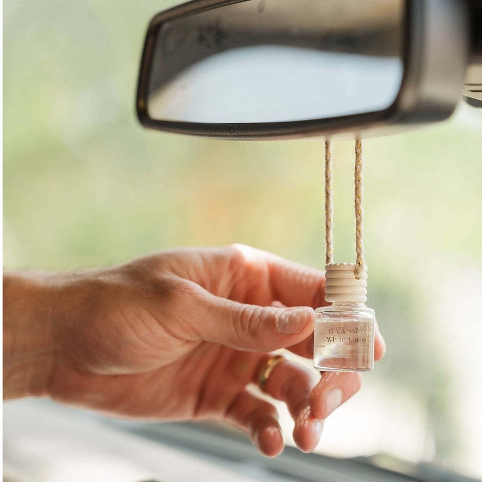 White Lotus car diffuser hanging from rearview mirror in vehicle interior