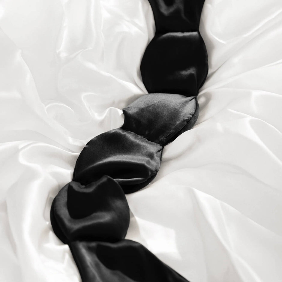 Black silk weighted sleep mask displayed on white tulle fabric, showing luxurious texture and design