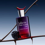 Juliette Has A Gun Purple Trouble bottle topped with a red chili pepper beside a blackberry on a thorny branch