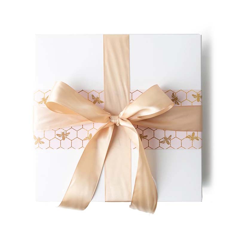 Gift box with golden bees on a pale blush sleeve and a glamorous gold satin bow.