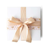 Gift box with golden bees on a pale blush sleeve and a glamorous gold satin bow.