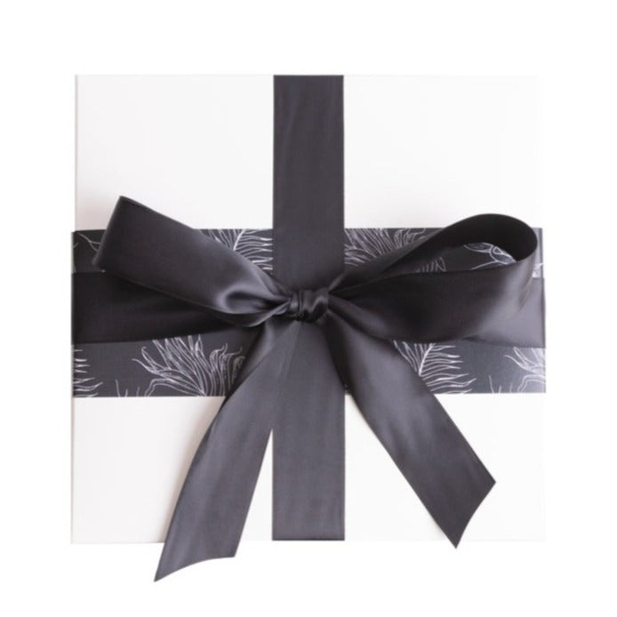 Gift box with illustrated pampas grass on a textured black background and a glamorous black satin bow.